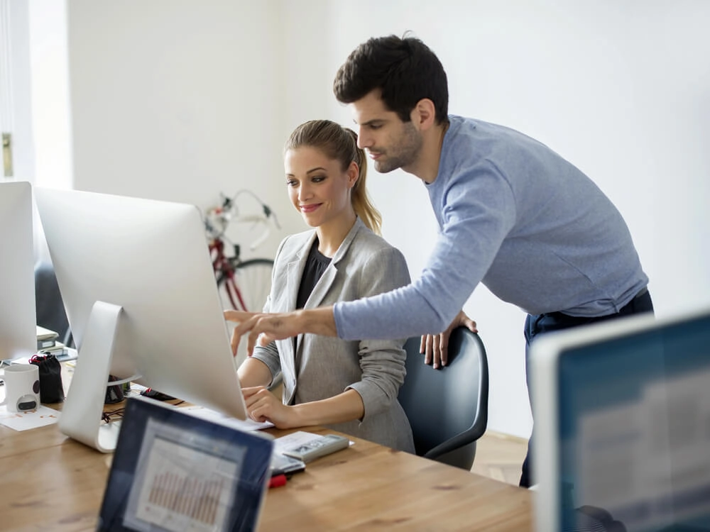 Bespoke, private training - a trainer points to the screen to demonstrate to his learner, the image shows the back of a computer screen with the female learner and male trainer both facing the screen