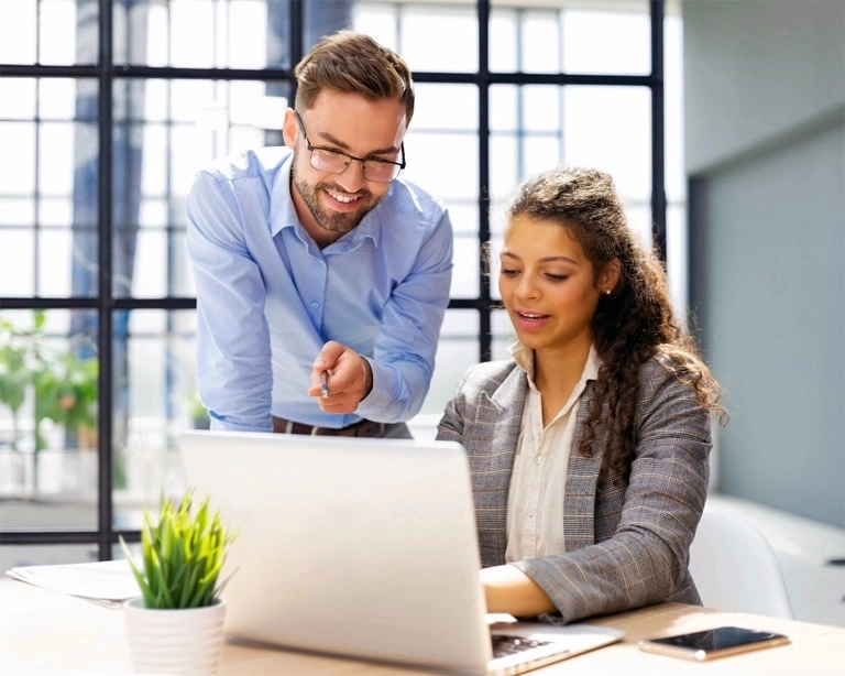 A Platform Training Instructor teaches a client who is sitting at a desk using her laptop.